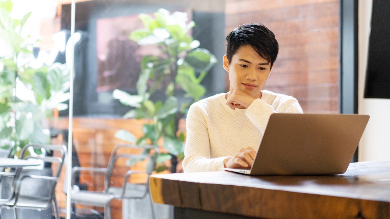 A man is using laptop in a coffee shop; image used for HSBC Malaysia beware of scams and fraud article page.