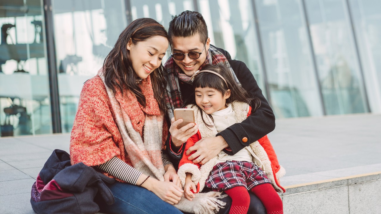 A little girl and her parents are looking at the mobile happily; image used for HSBC Malaysia protect what matters article page.