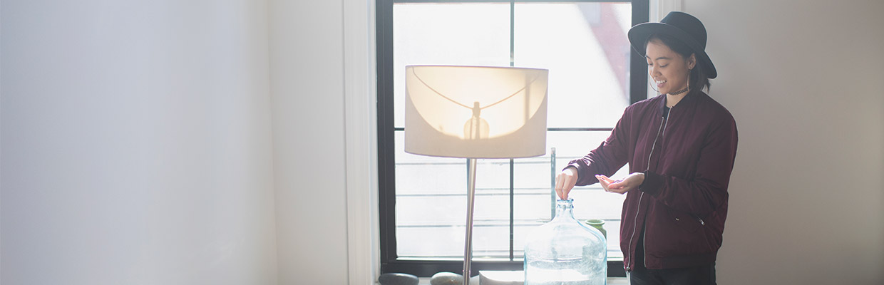 A woman is putting money in a jar; image used for HSBC Basic Savings Account page.