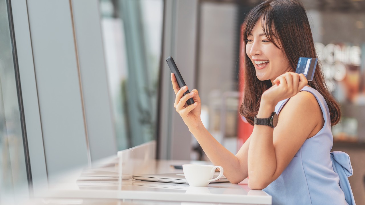 smiling girl with card and looking her mobile; image used for HSBC Malaysia Credit Cards 11 tips to get the most out of 11.11