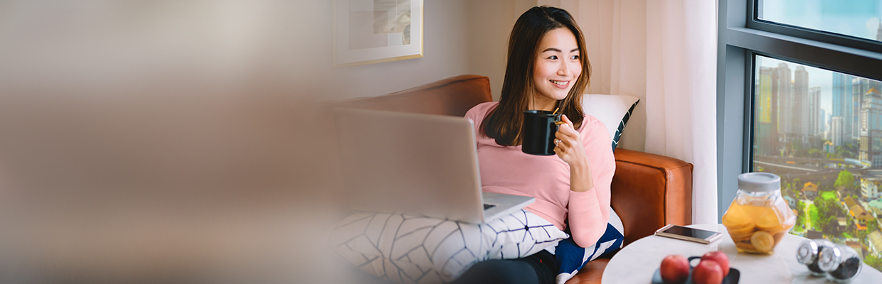 A women is using laptop and drinking coffee in the living room; image used for HSBC Malaysia Auto Balance Conversion page.