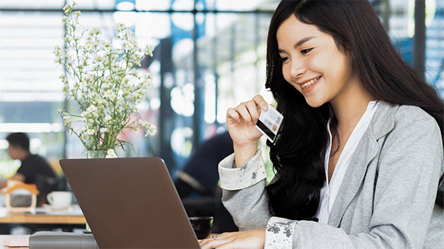 A woman using laptop and handling a credit card in her hand; image used for HSBC Malaysia credit limit increase article page