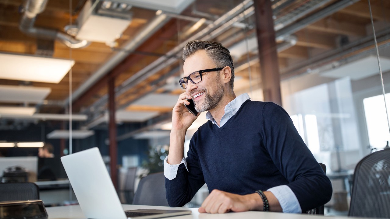 Guy dressed in a sweater sitting at his desk in front of a laptop while speaking on a phone. Image used for HSBC Malaysia JomPay page.