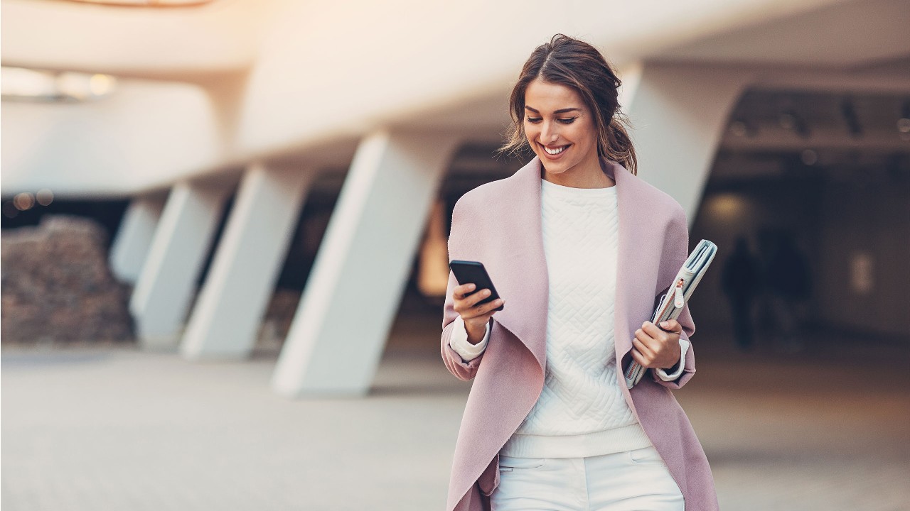 Woman in a pink blaze holding her phone walking outside. Image used for HSBC Malaysia bank onlinr page.