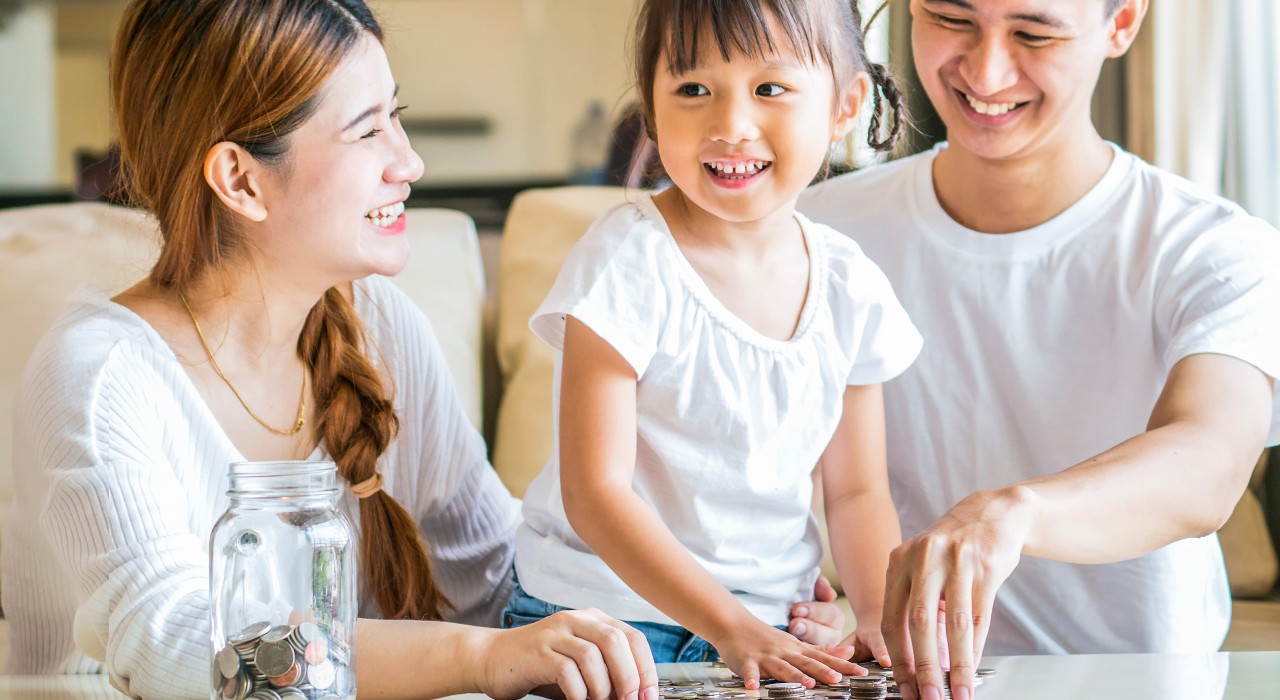 A little girl and her parents are smiling happily; image used for HSBC Malaysia financial education for kids article page.