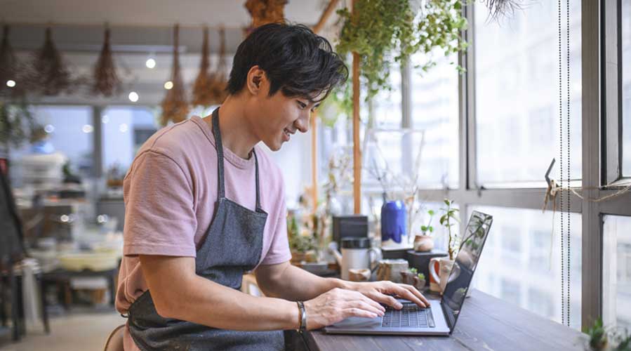 A coffee shop owner is using his laptop; image used for HSBC Malaysia Fusion ‘Managing cash flow for SME in challenging times’ article.